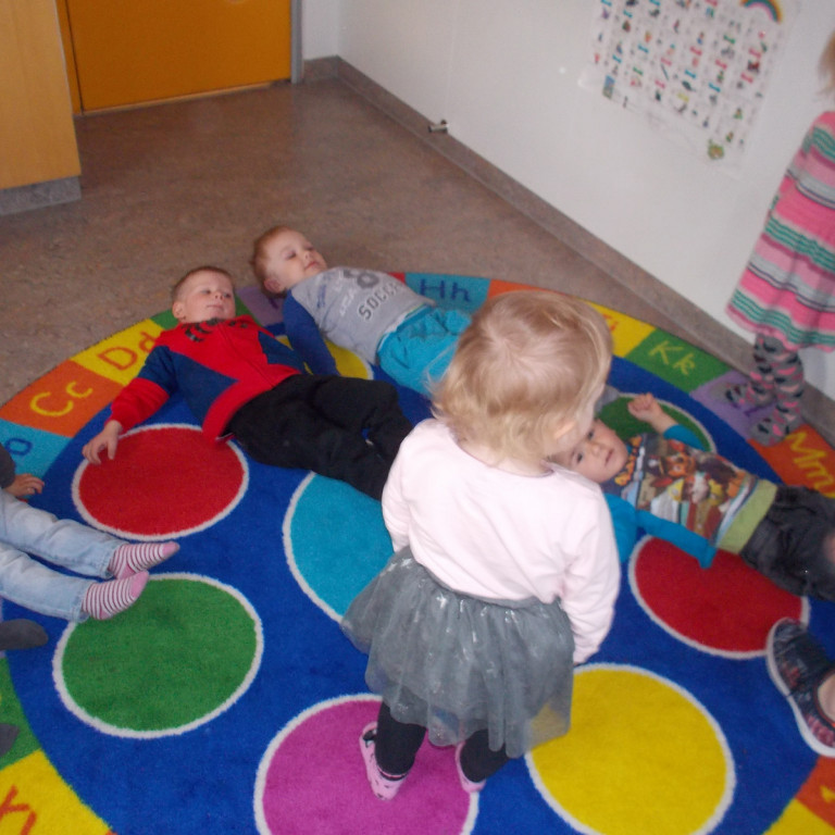 Börnin raða sér með hjálp kennara á gólfið og mynda bókstafin A með líkamanum